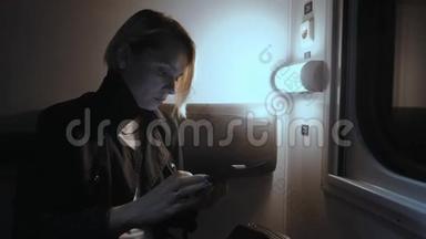 那个女孩晚上在火车上。 坐在火车上用智能手机